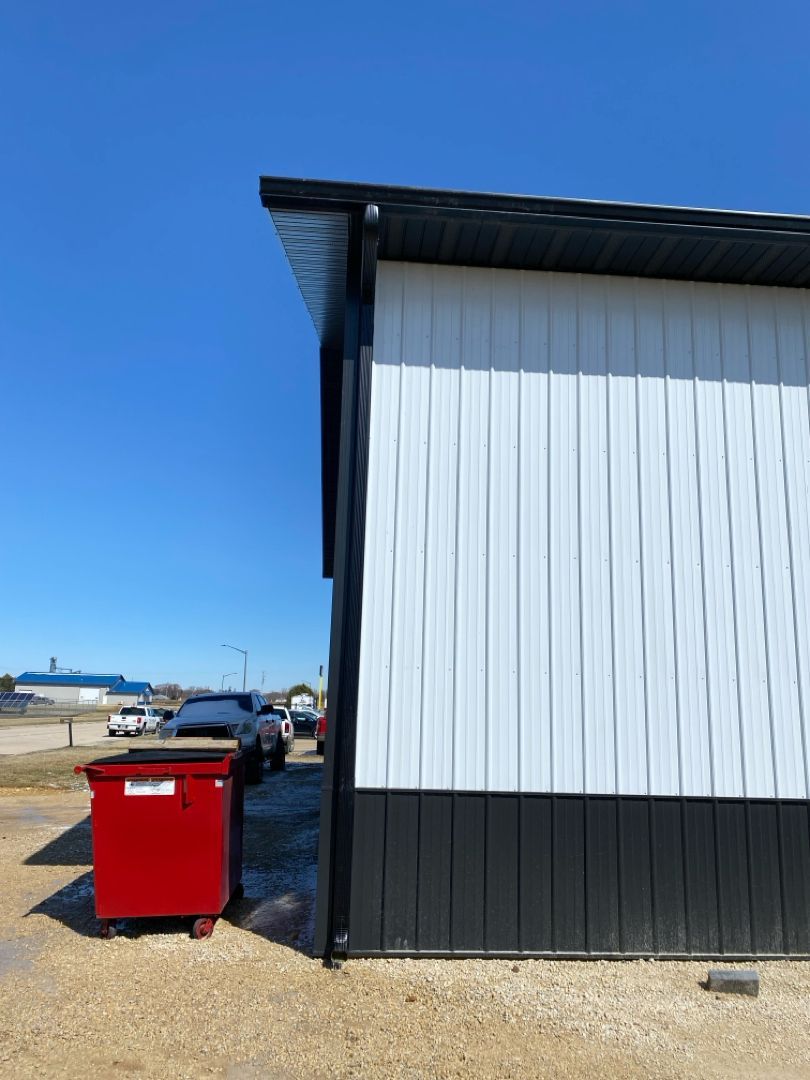 A red dumpster is parked in front of a white and black building.