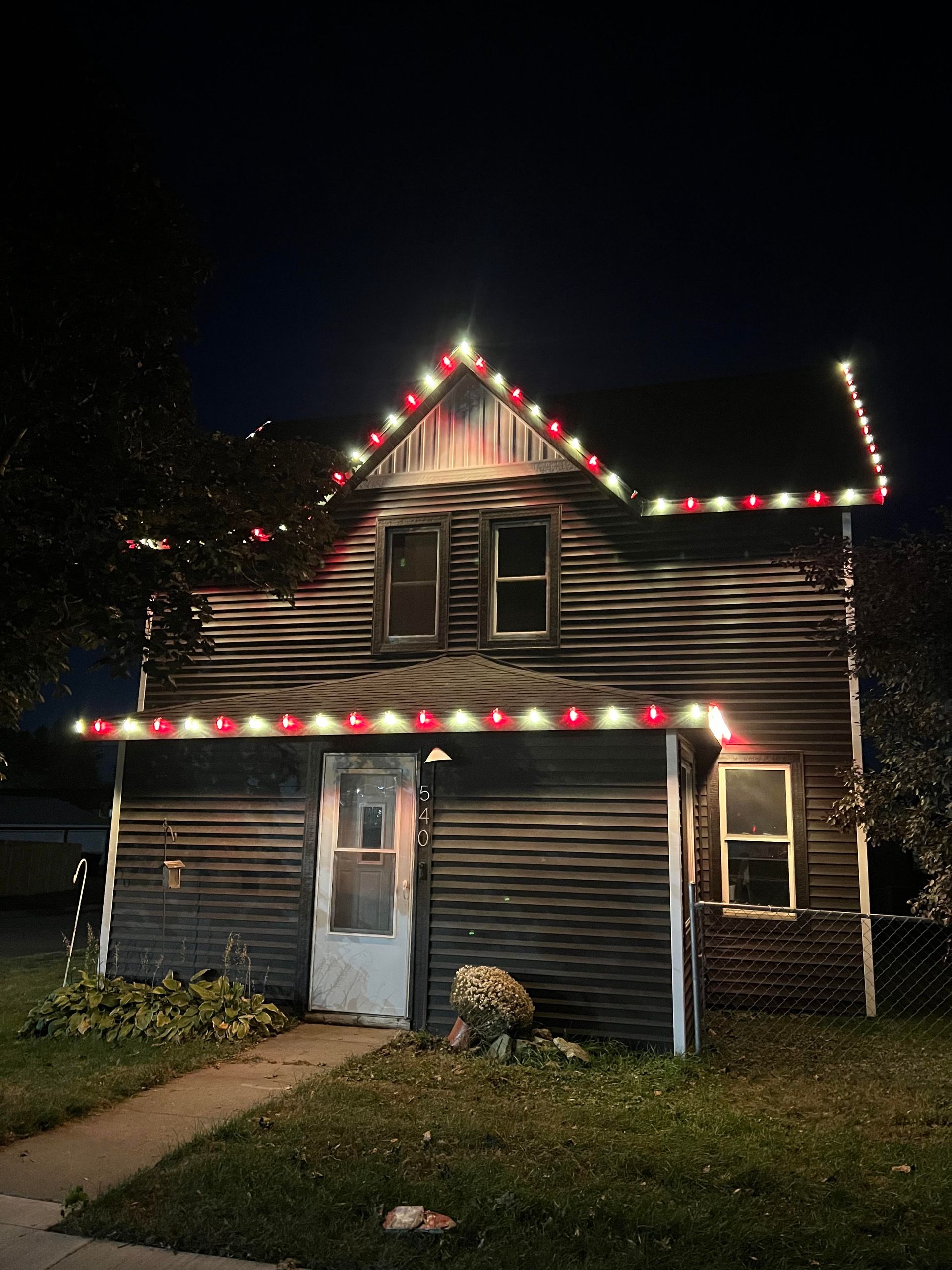 A house with Christmas lights on the roof is lit up at night.