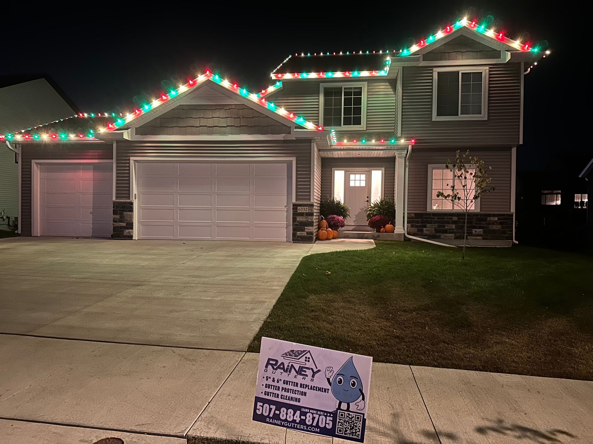 A house with Christmas lights on the roof and a sign in front of it.
