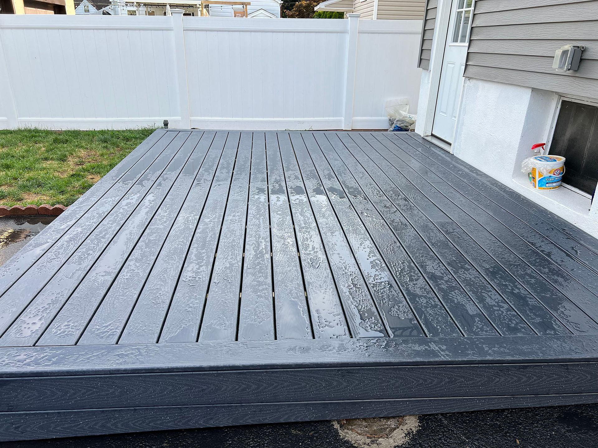 A gray wooden deck with a white fence in the background.