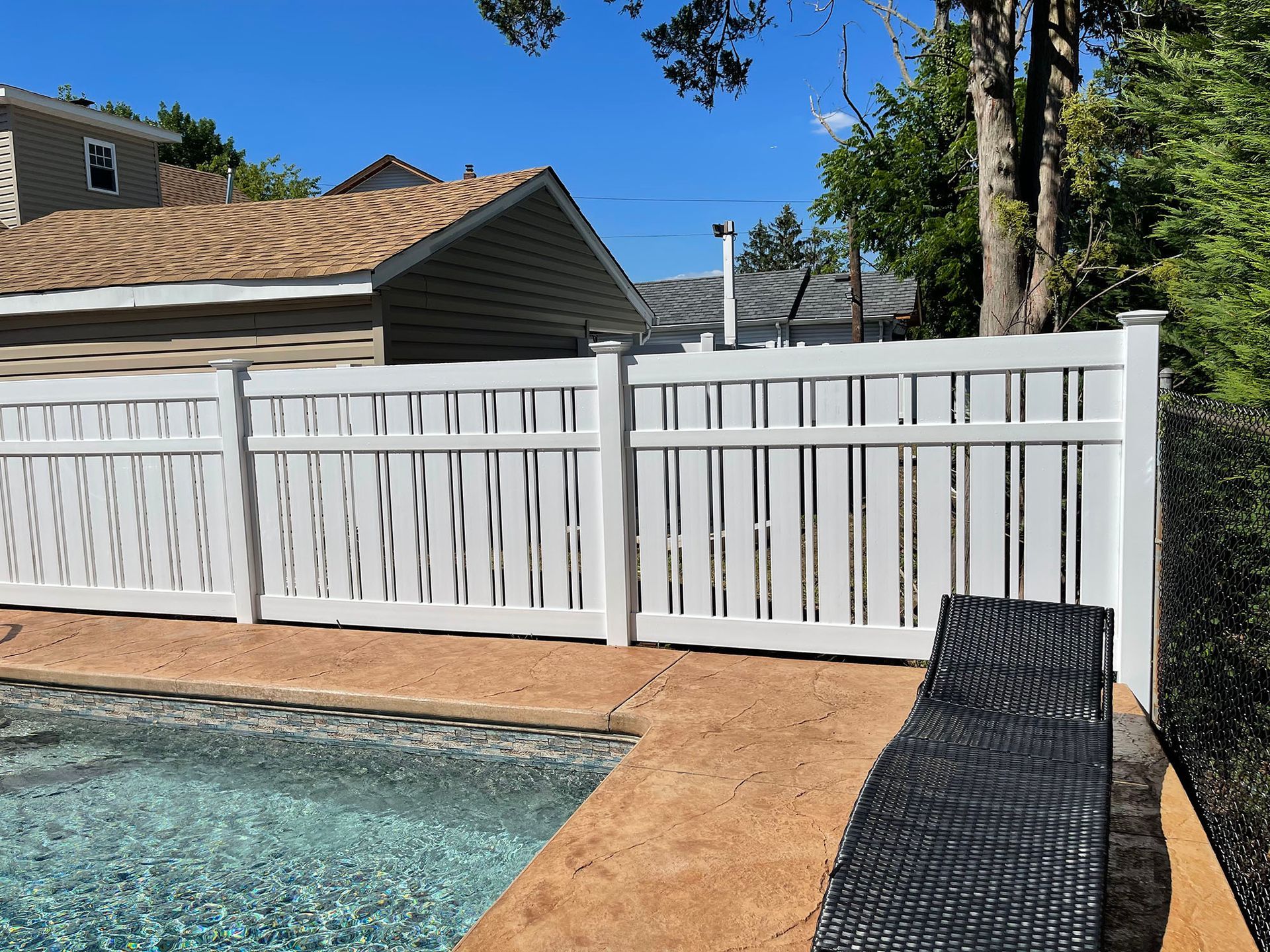 A white fence surrounds a swimming pool in a backyard.