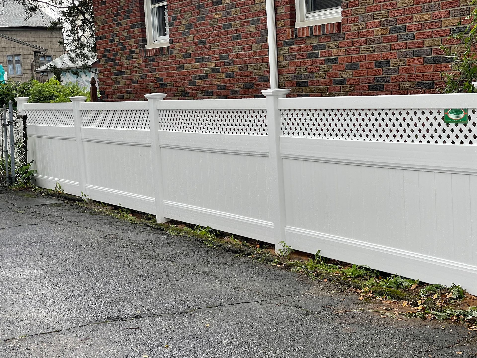 A white fence is sitting on the side of a road in front of a brick house.