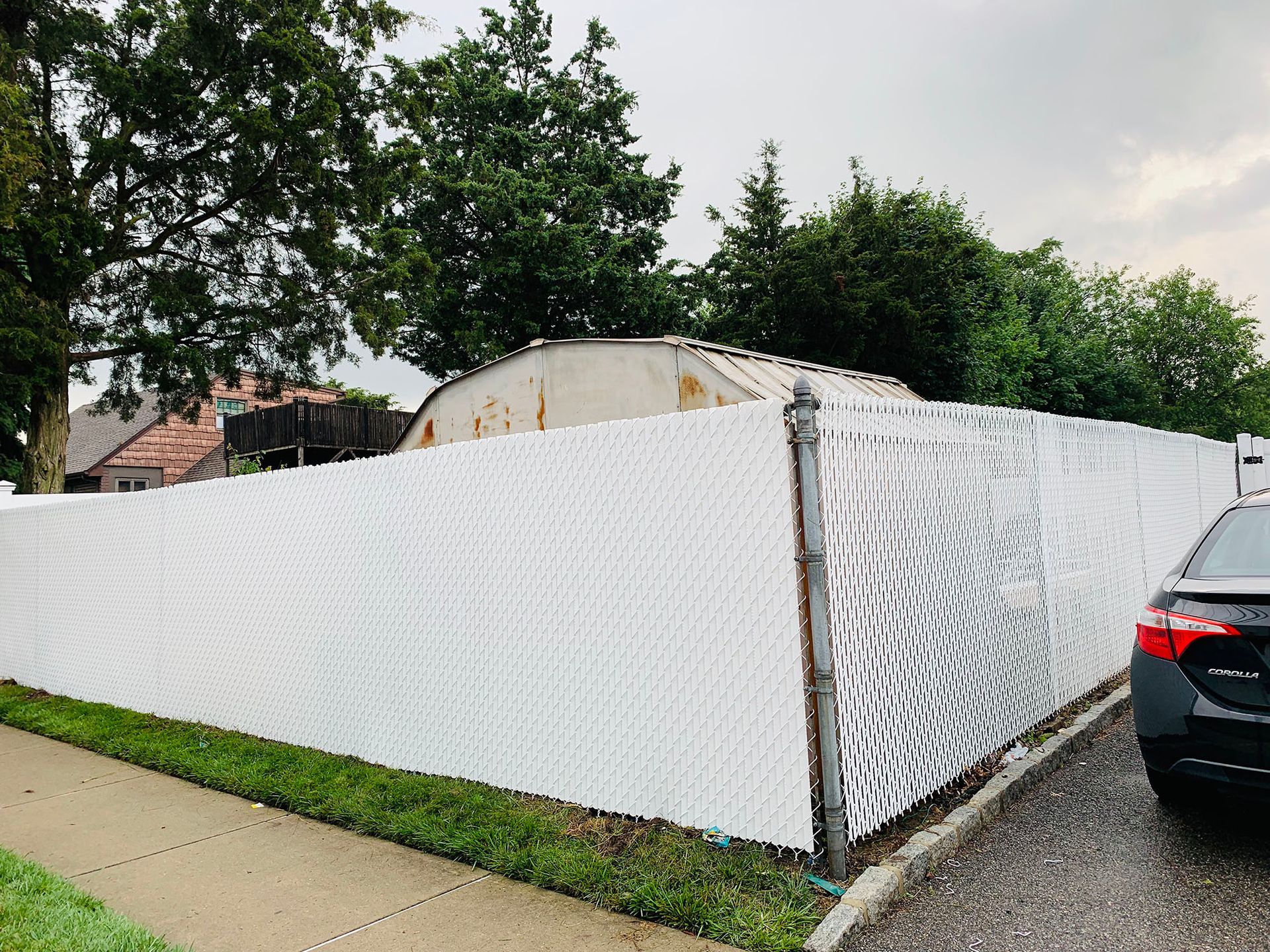 A car is parked in front of a white chain link fence.