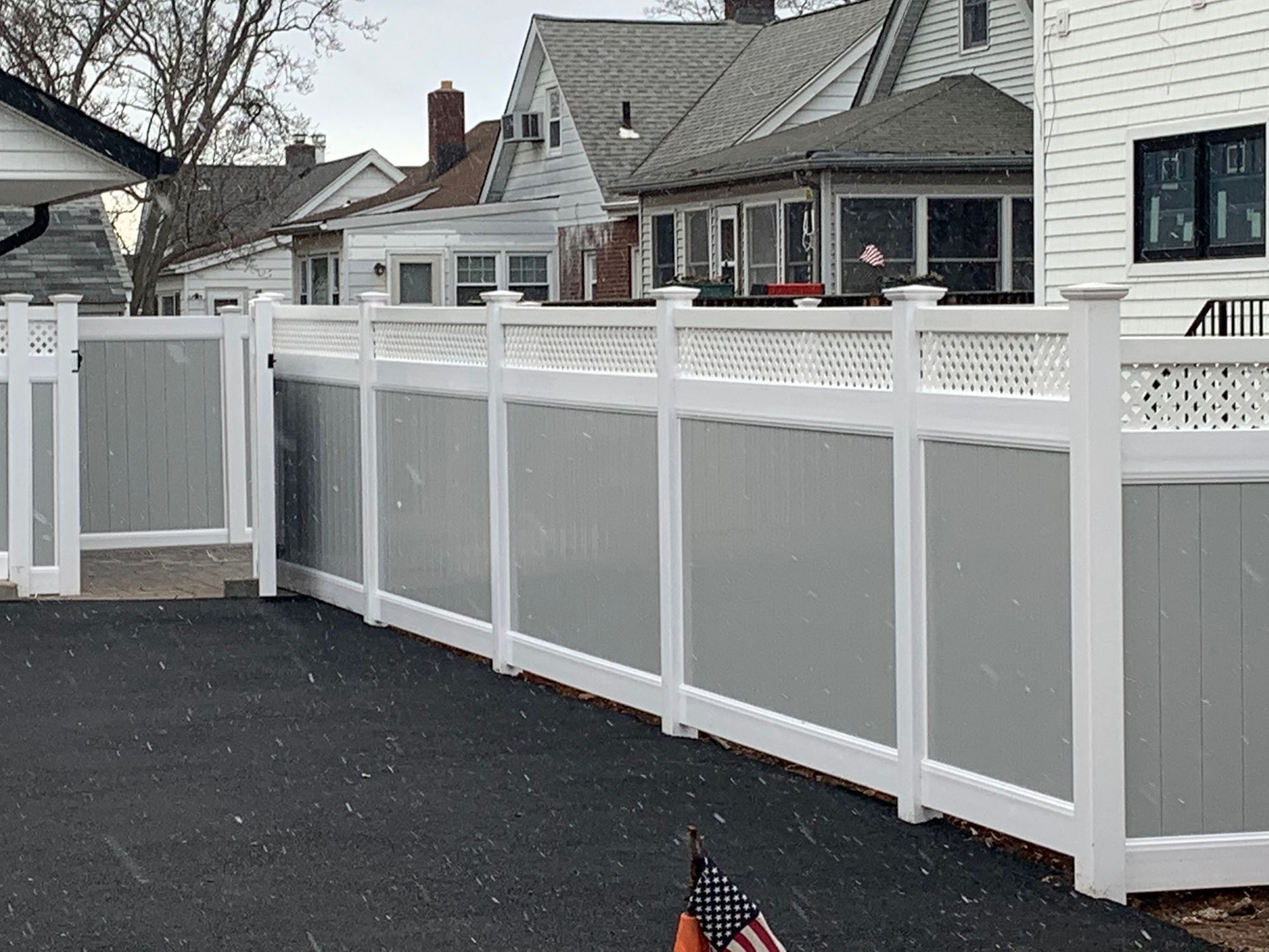 A gray and white fence surrounds a driveway in front of a house.