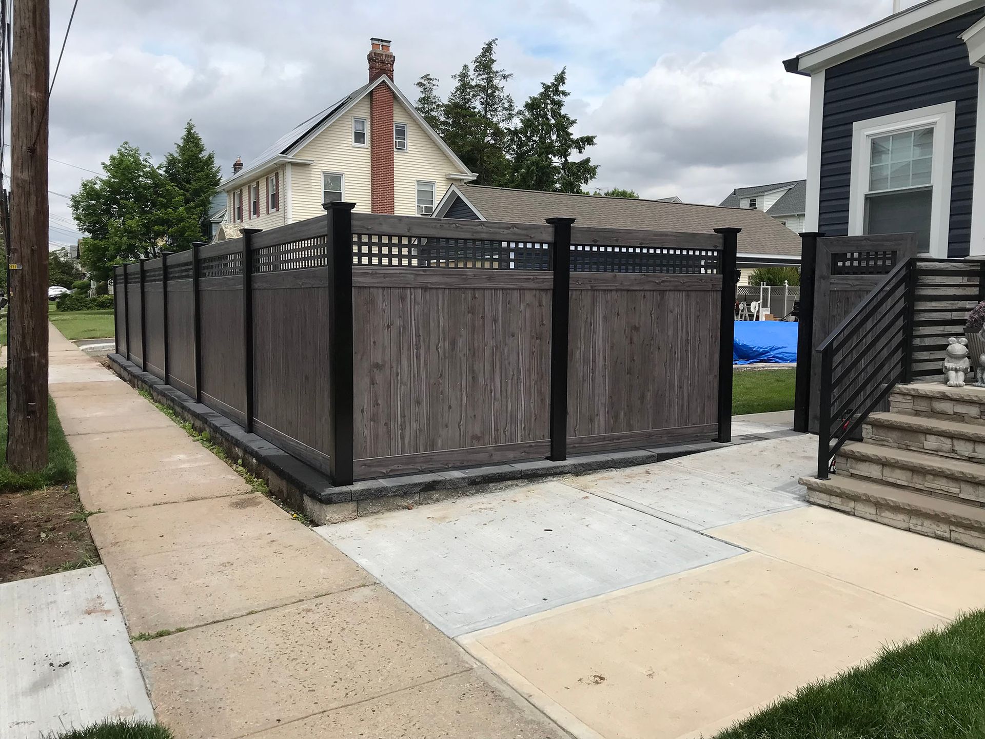 A wooden fence is along the sidewalk in front of a house.