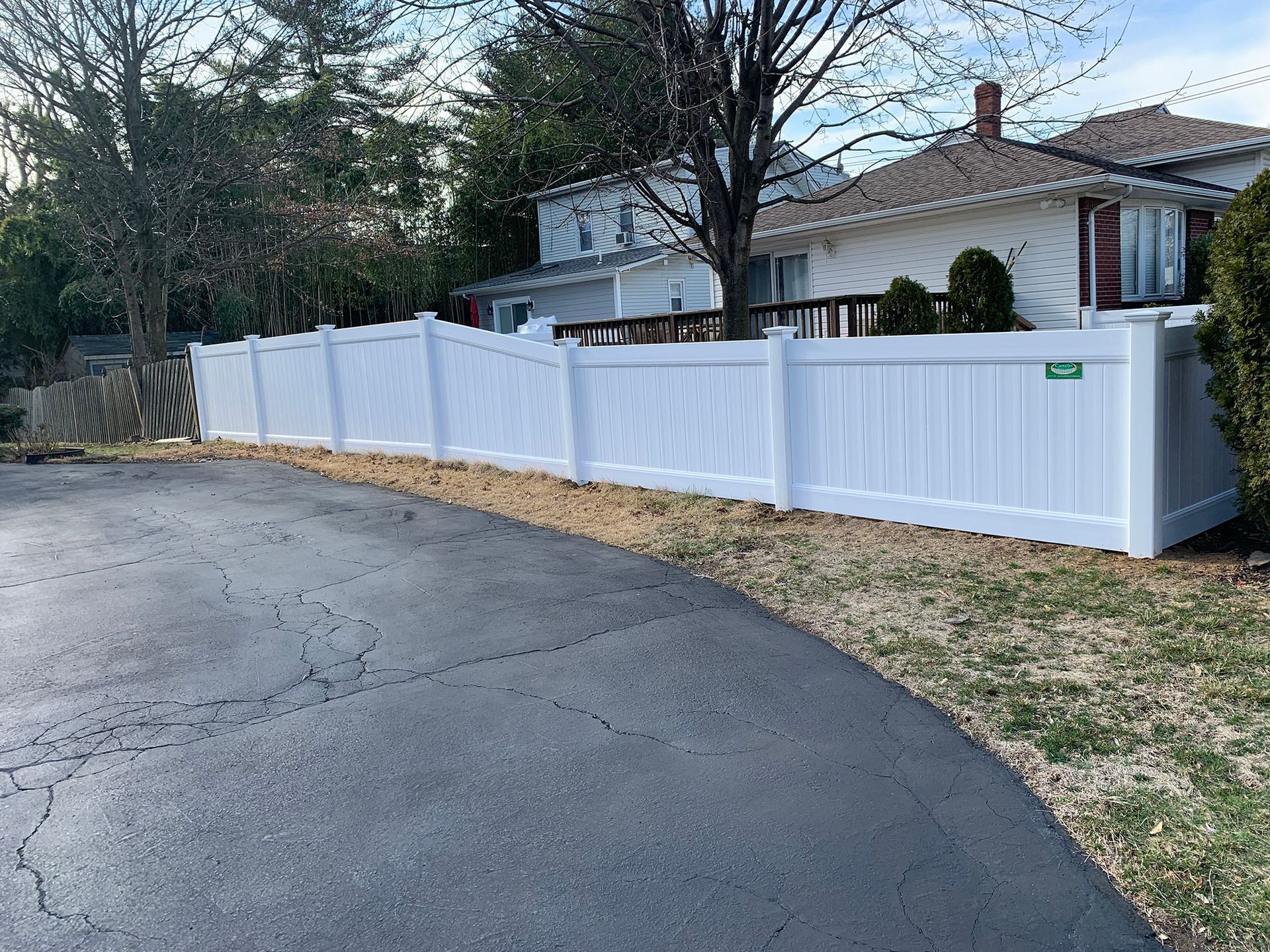 A white vinyl fence surrounds a driveway in front of a house.
