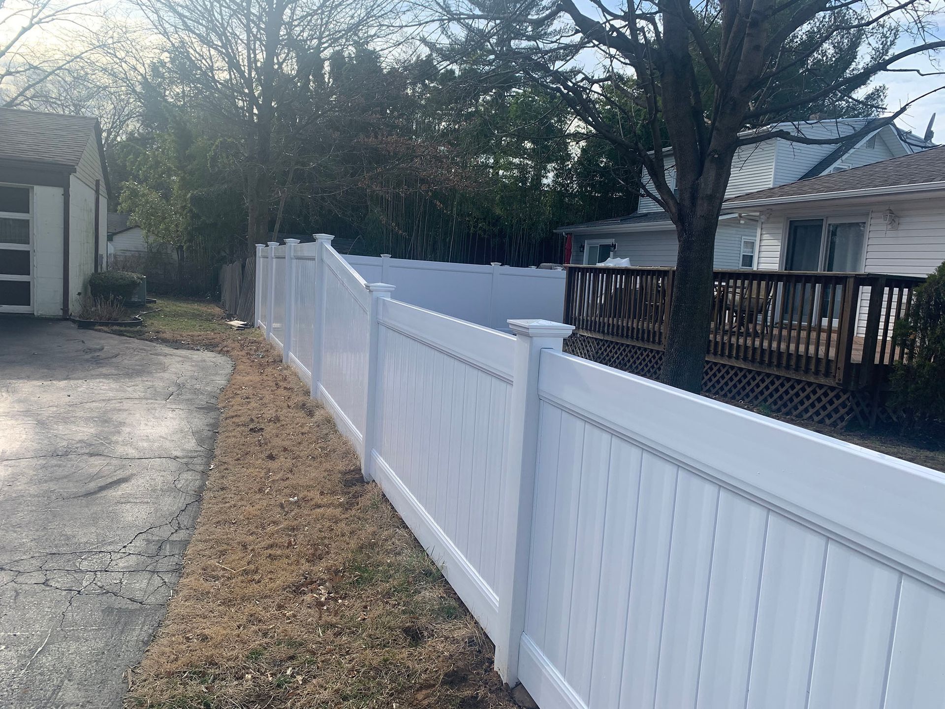 A white fence is surrounding a house and a driveway.