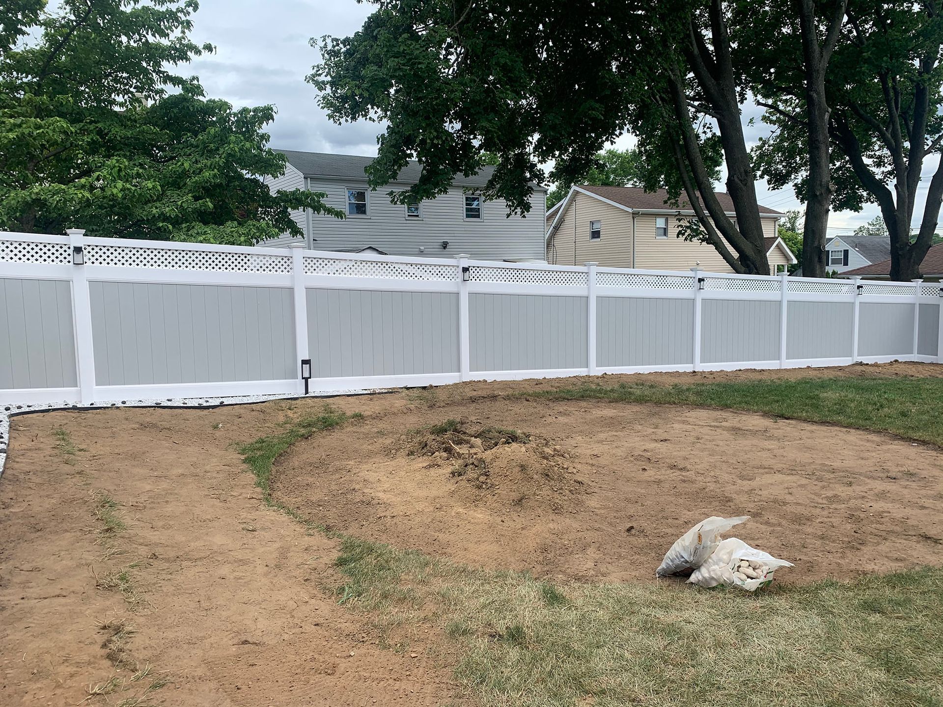 A white fence surrounds a dirt field in a backyard.