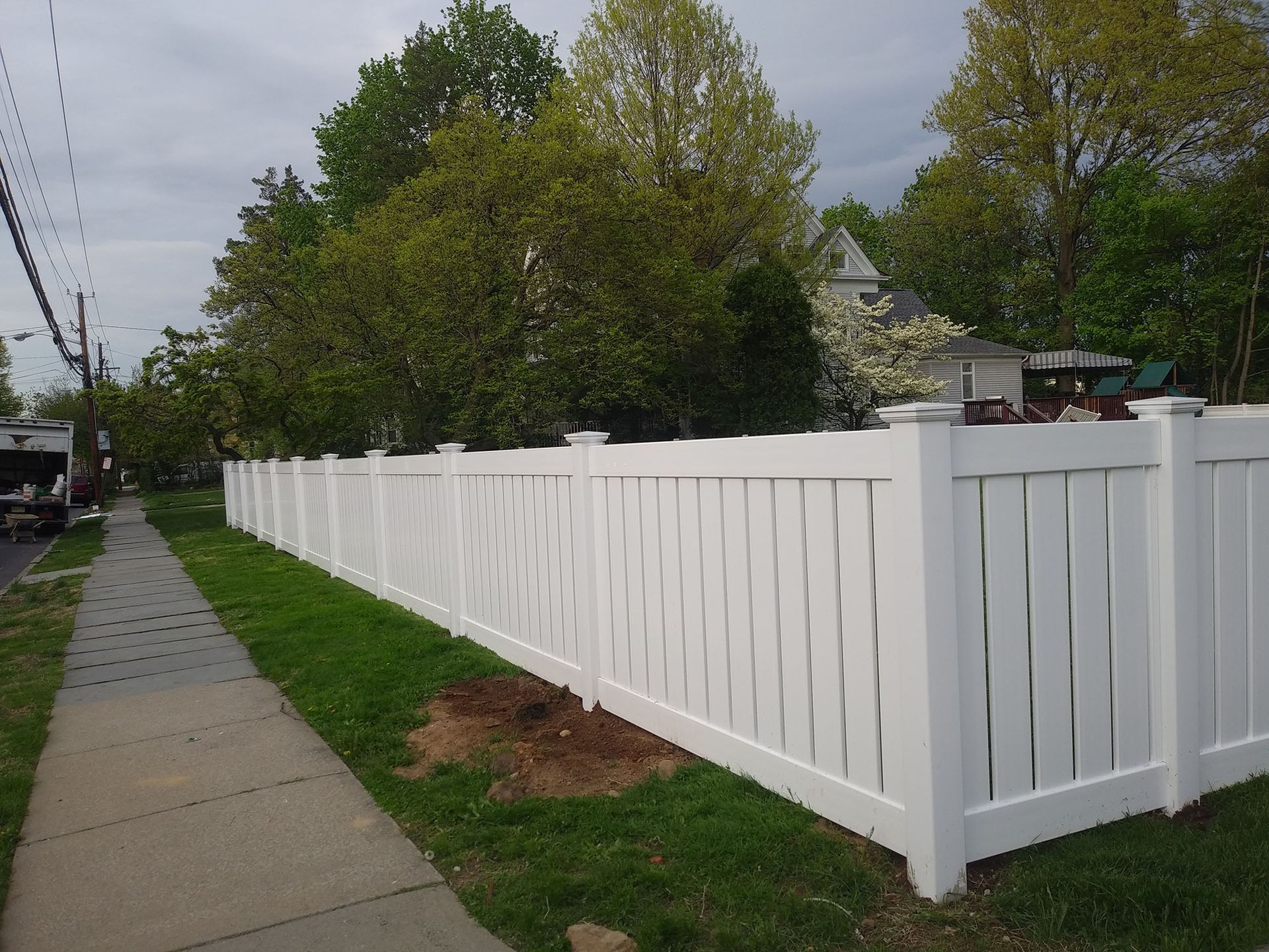 A white fence is along the side of a sidewalk.