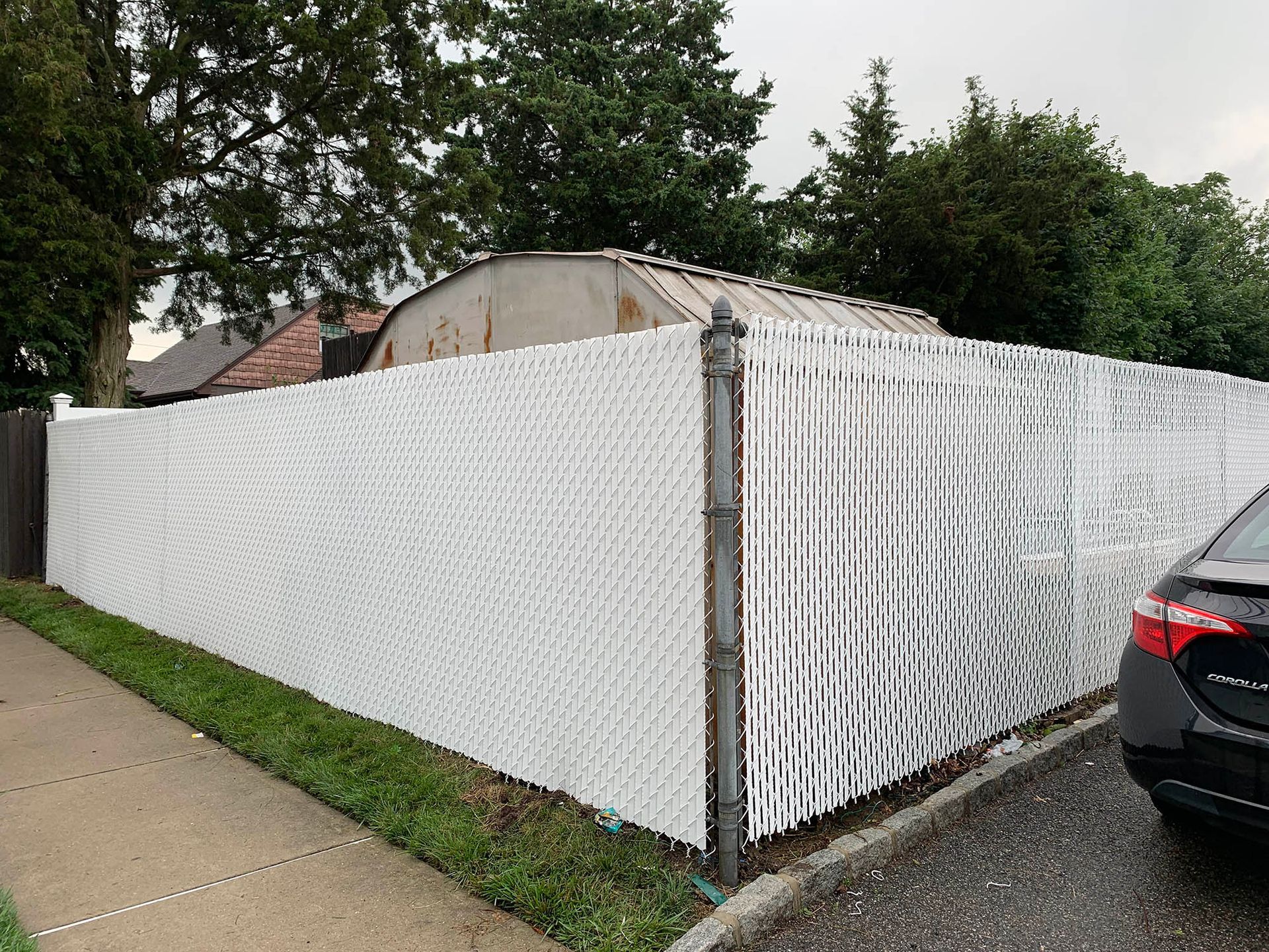A white chain link fence with a car parked in front of it.