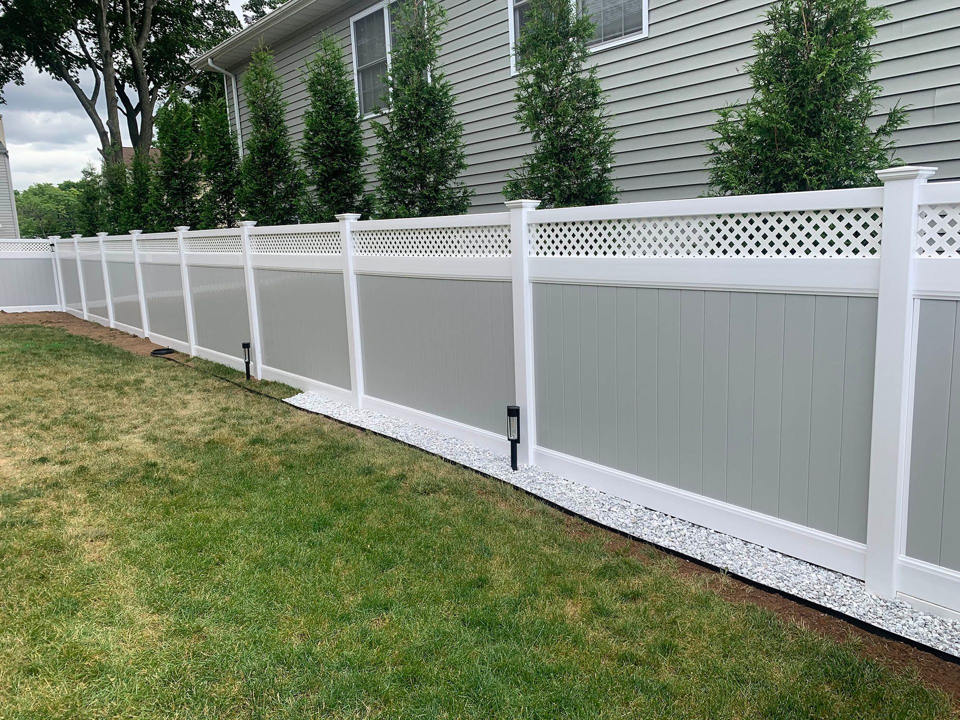 A white fence surrounds a lush green yard in front of a house.