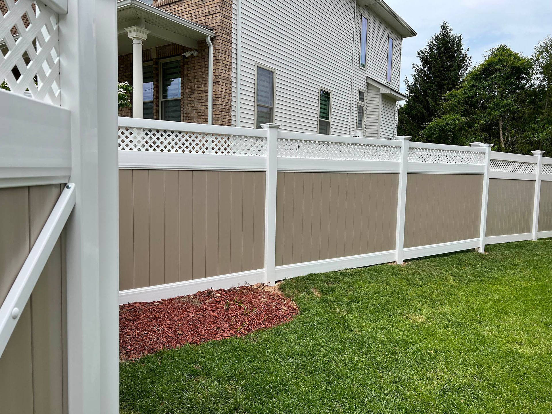 A white and brown fence is in the backyard of a house.
