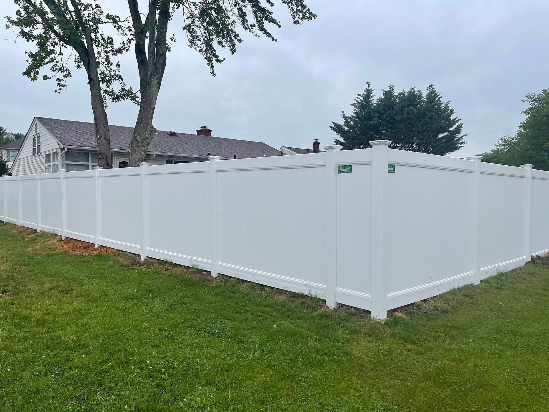 A white fence surrounds a lush green field in front of a house.