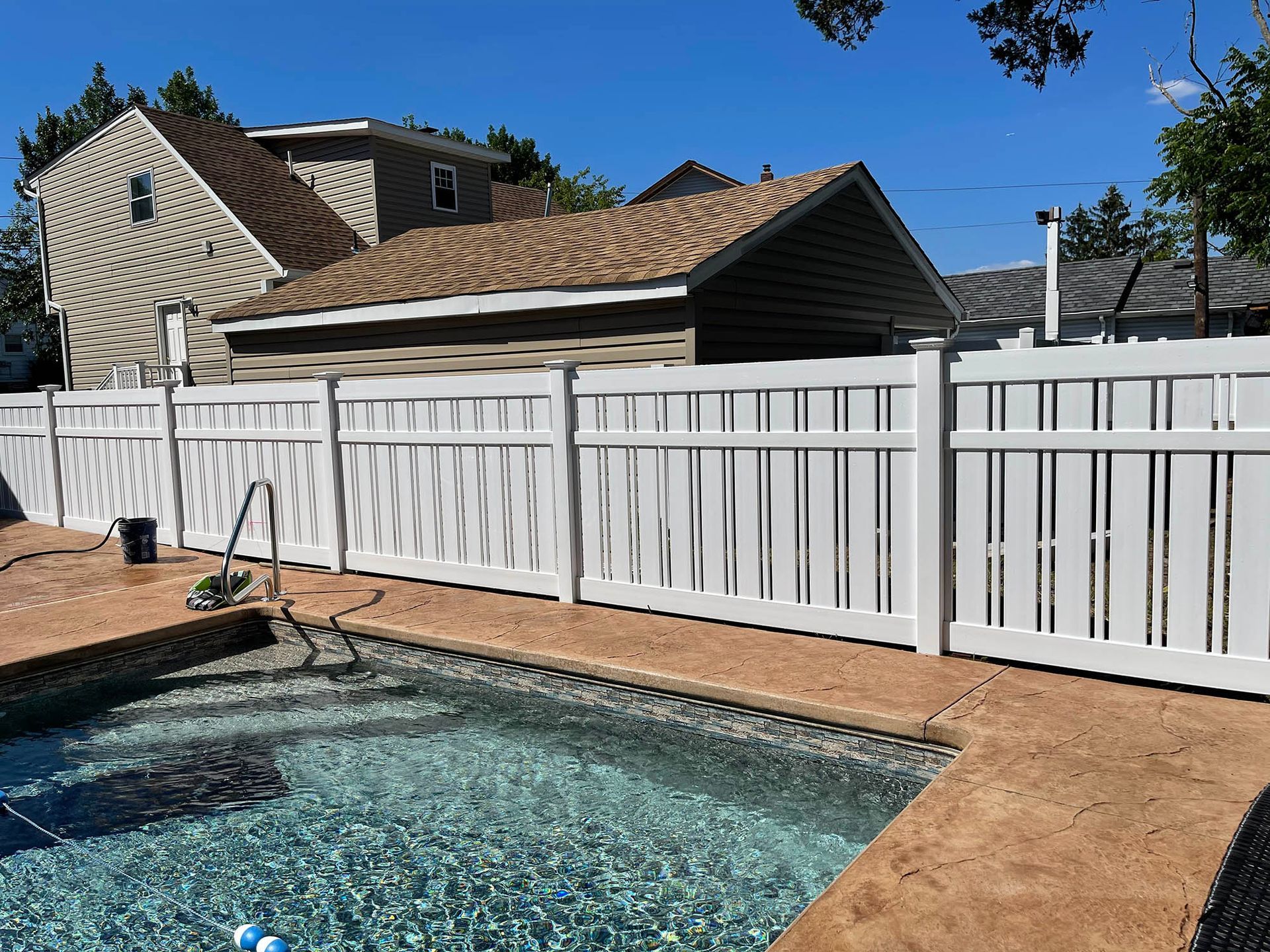 A white fence surrounds a swimming pool with a house in the background.
