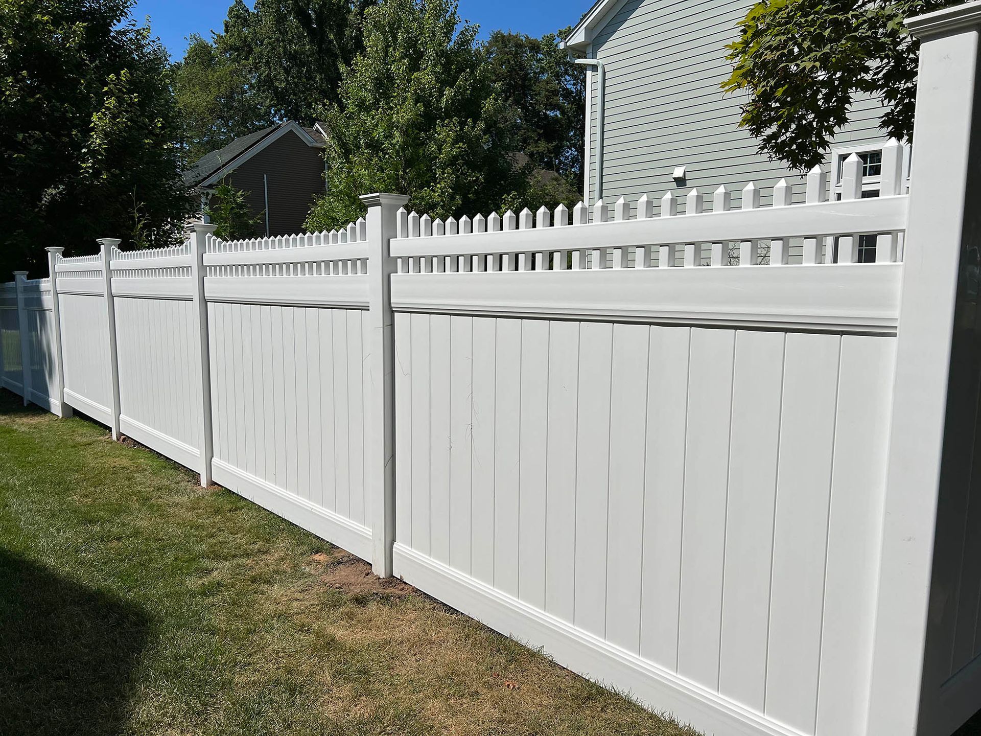 A white vinyl fence is sitting in the grass in front of a house.