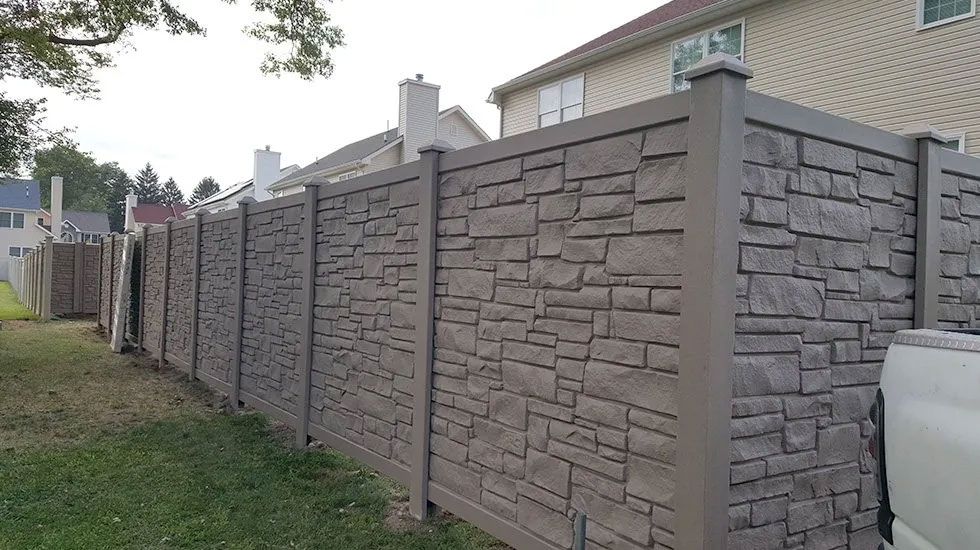 A stone fence is surrounding a yard in front of a house.