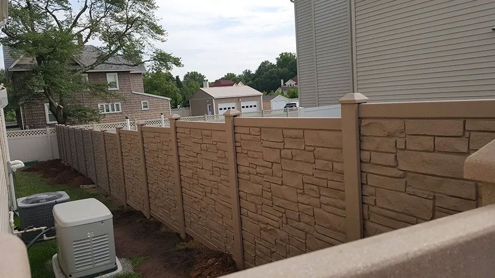 A concrete fence surrounds a backyard with a house in the background.