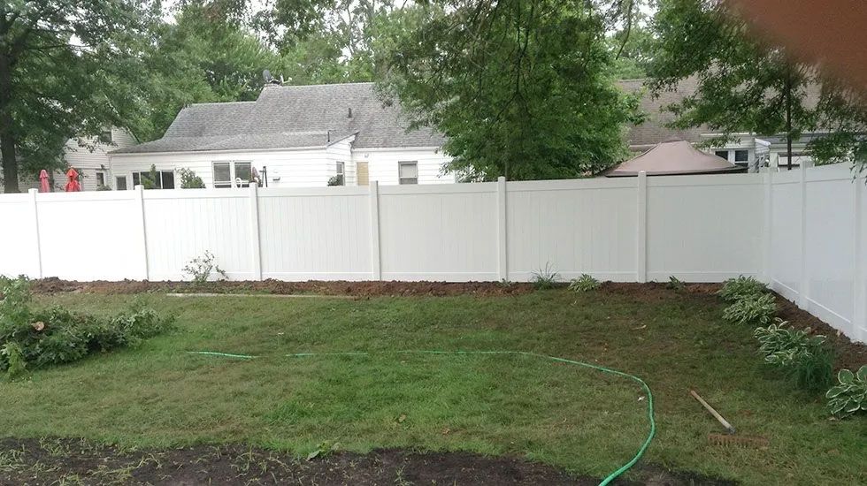 A backyard with a white fence and a green hose.