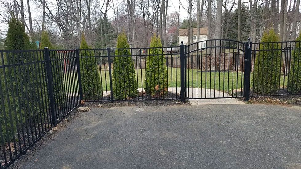 A black metal fence surrounds a driveway with trees in the background.