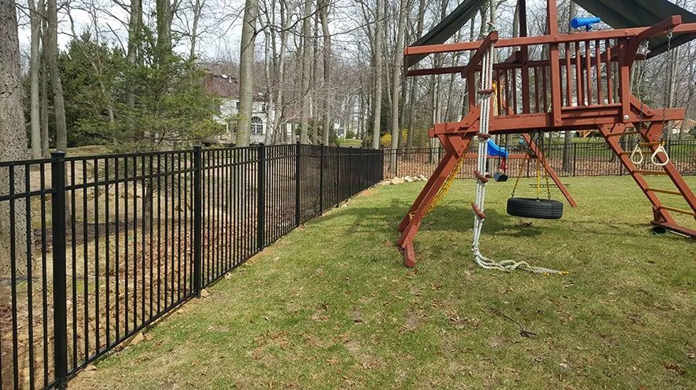 A backyard with a playground and a black fence.