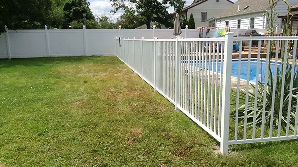 A white fence surrounds a swimming pool in a backyard