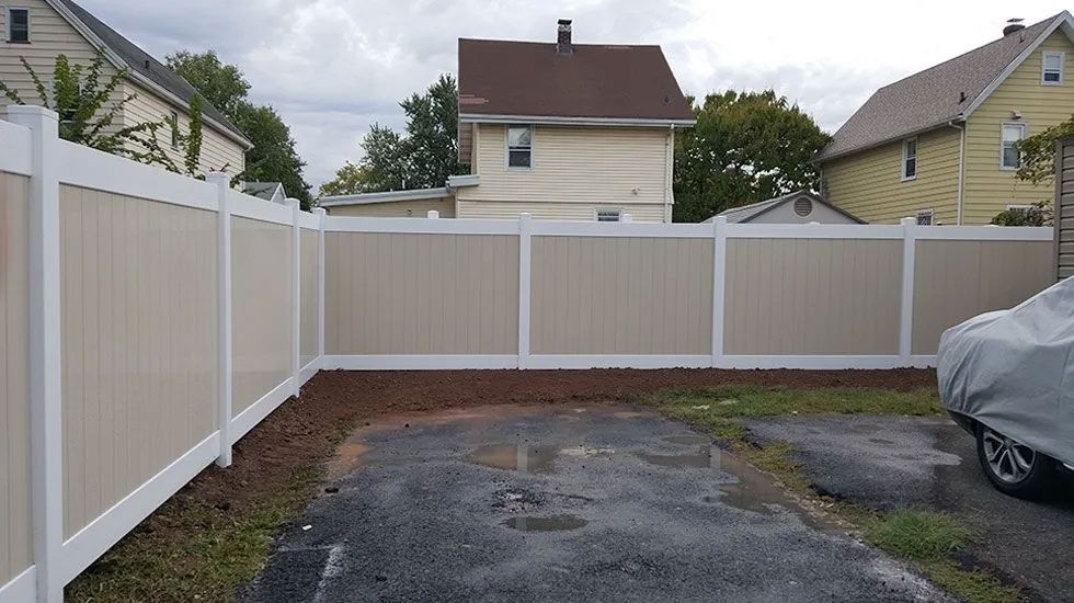 A white fence surrounds a driveway with a car parked in front of it.