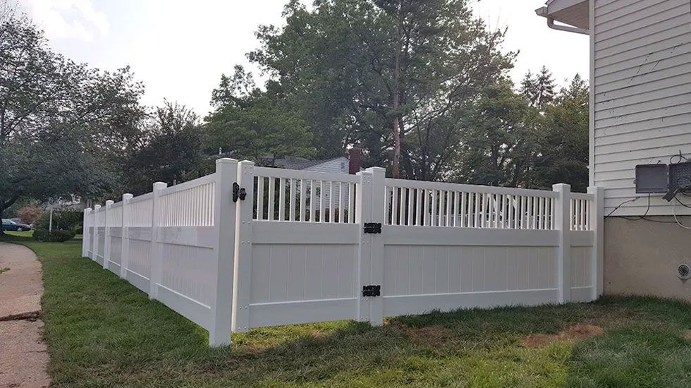A white vinyl fence is surrounding a house in a yard.