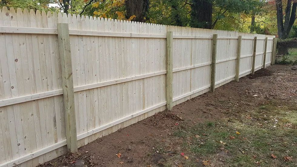 A white wooden fence with wooden posts in a backyard.
