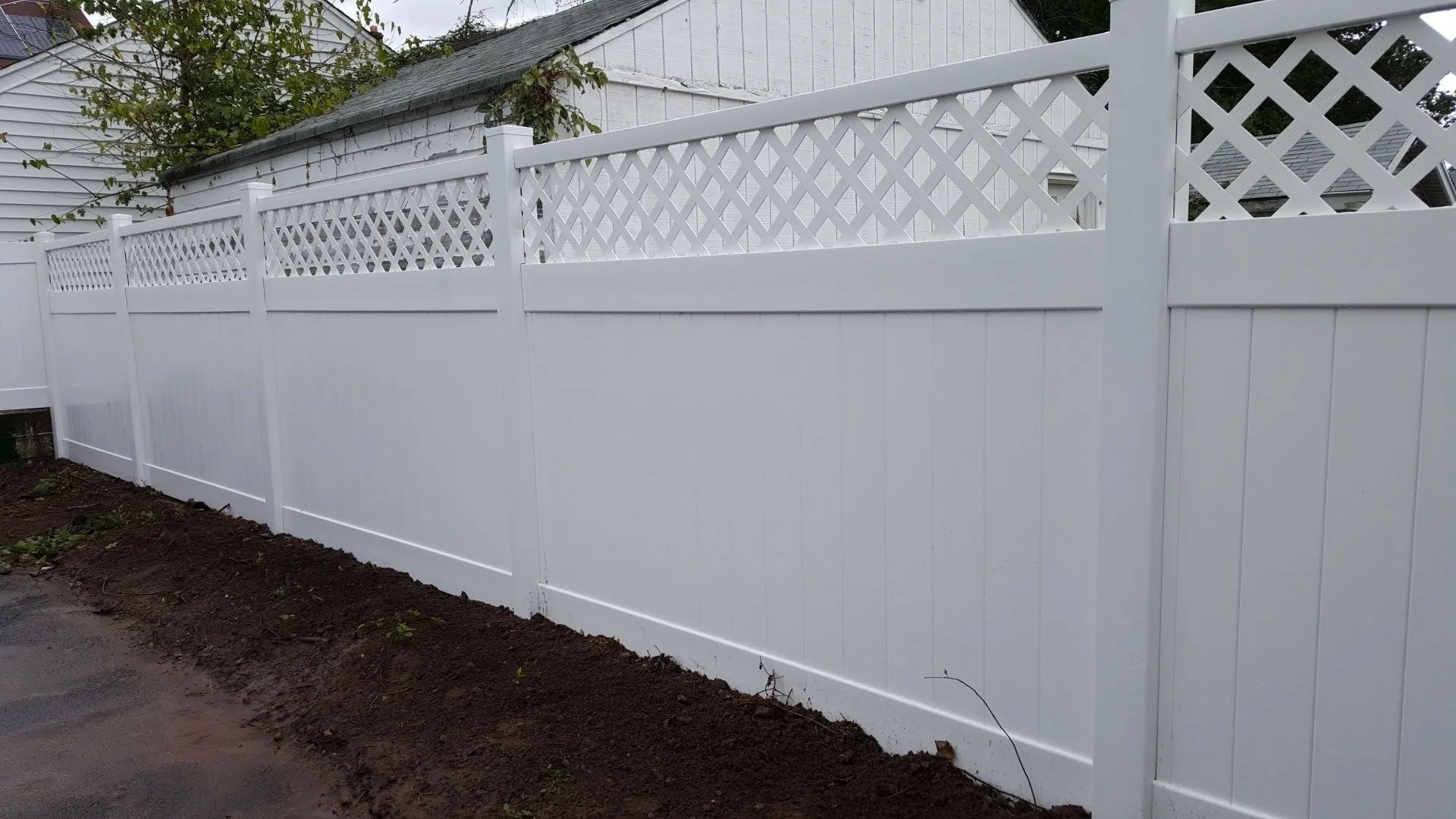 A white fence with a lattice design is sitting next to a house.