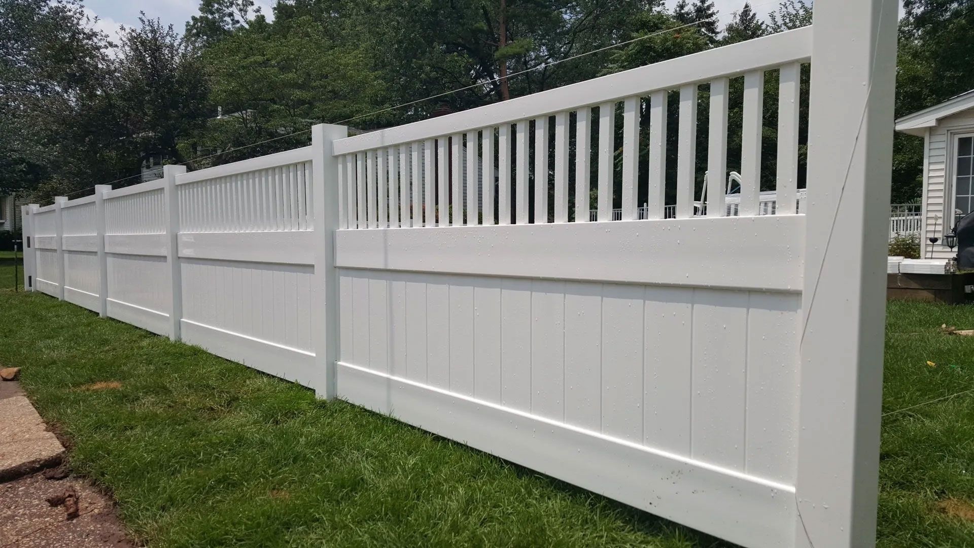 A white vinyl fence is sitting in the grass in front of a house.