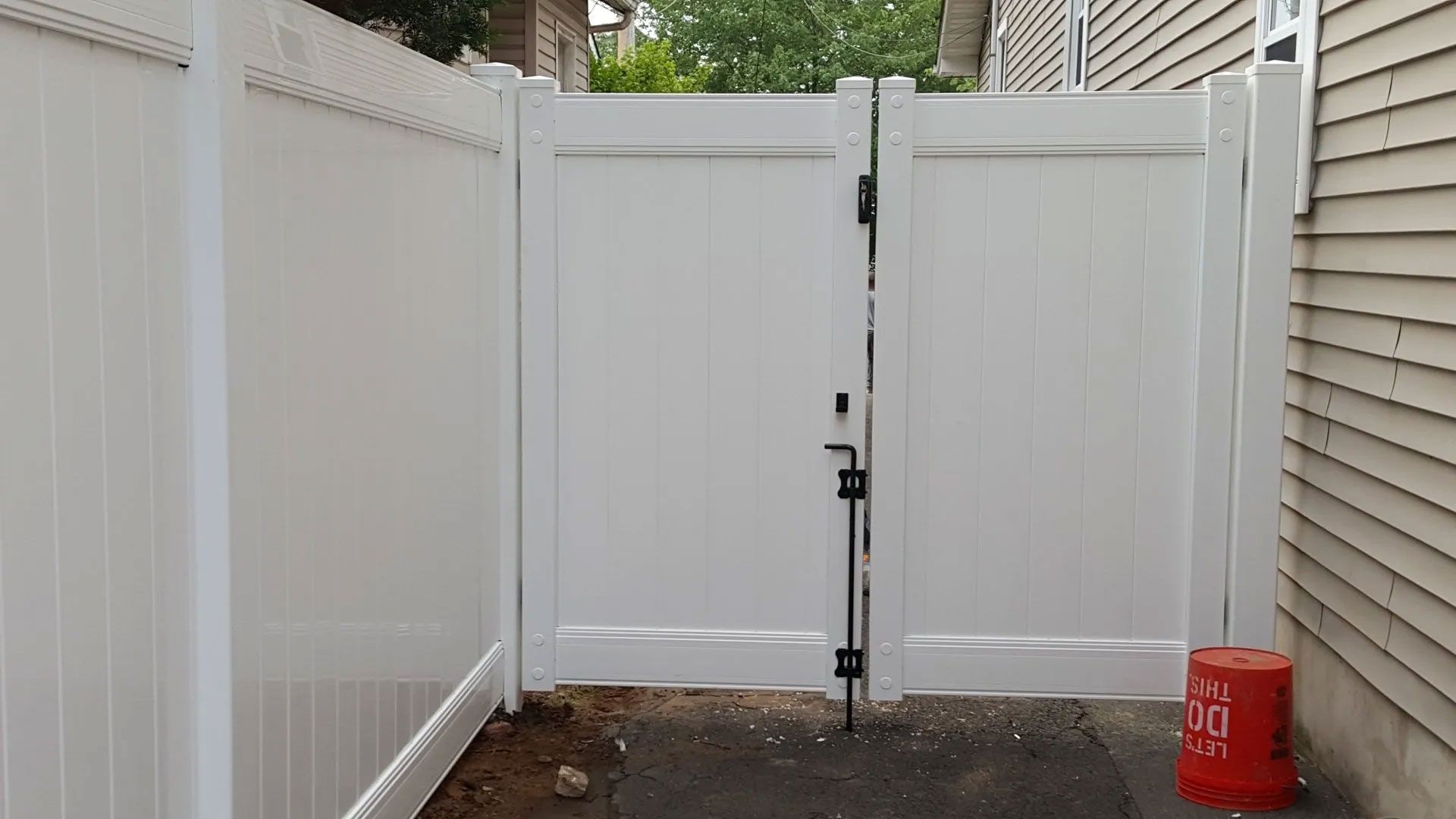 A white fence with a gate is next to a house.