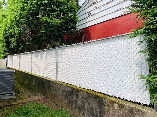 A white chain link fence is sitting next to a concrete wall.