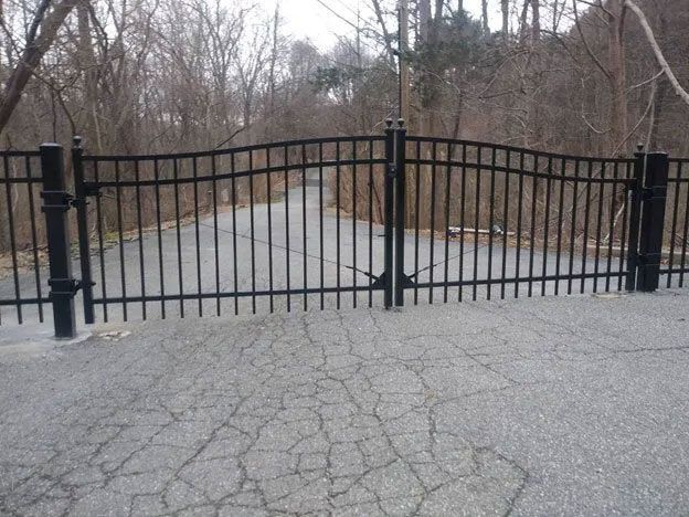 A black fence surrounds a road with trees in the background