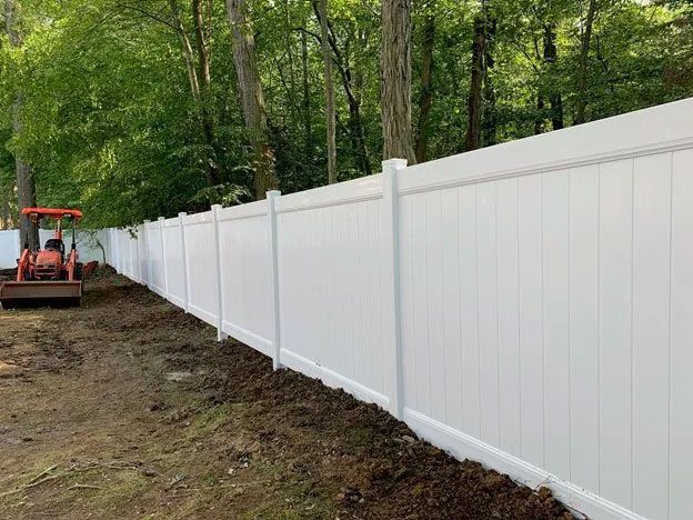 A white vinyl fence is being built in a backyard.