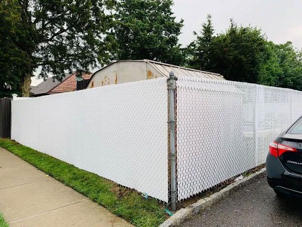 A white chain link fence with a car parked in front of it.