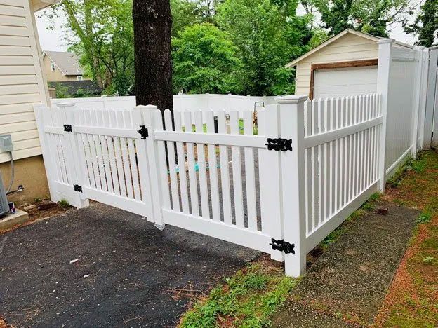 A white fence is sitting next to a garage in front of a house.
