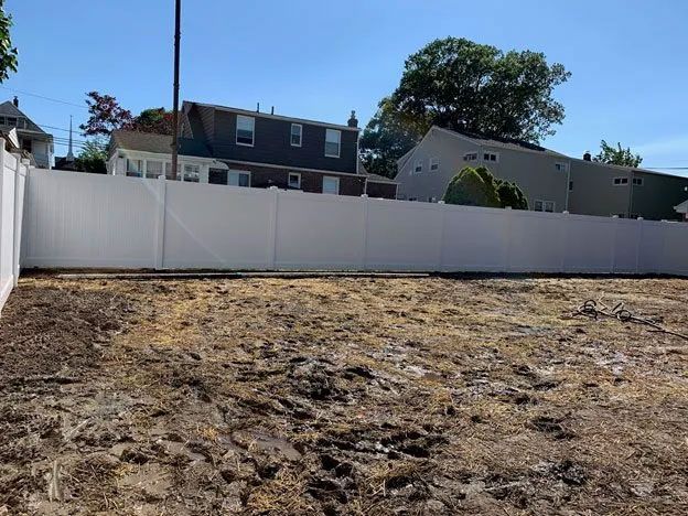 A white fence surrounds a dirt field in front of a house.