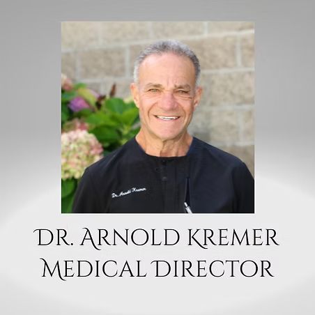 Dr. Arnold Kremer, Medical Director, smiling in a black shirt against a stone backdrop
