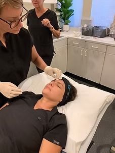 Facial treatment in a spa, with a client lying on a bed while a practitioner applies cream.