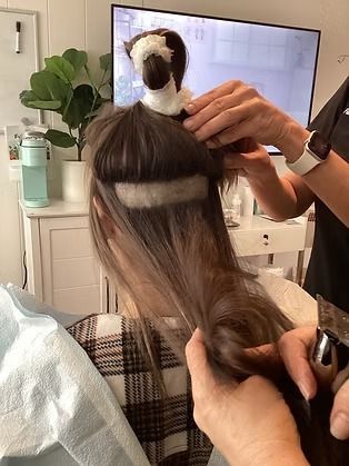 Stylist sections and clips a client’s brown hair in a salon with a mirror and TV in the background