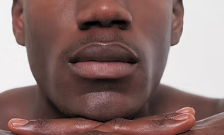 Close-up of a person resting their chin on folded hands, with a neutral expression on a white background