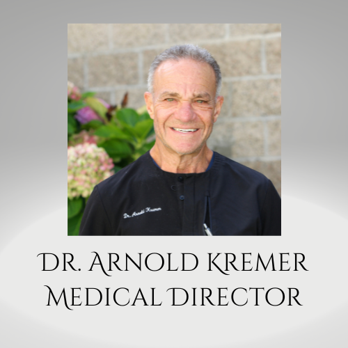 Portrait of Dr. Arnold Kremer, Medical Director, in a black coat against a stone wall and flowers