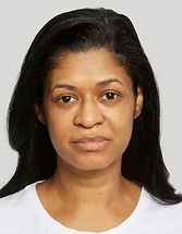 Head-and-shoulders portrait of a woman with dark hair, wearing a white top on a plain gray background