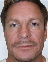 Close-up portrait of a man with short hair and a mustache, looking straight ahead against a plain background
