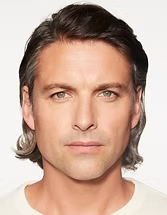 Close-up portrait of a person with short dark hair and a neutral expression on a white background