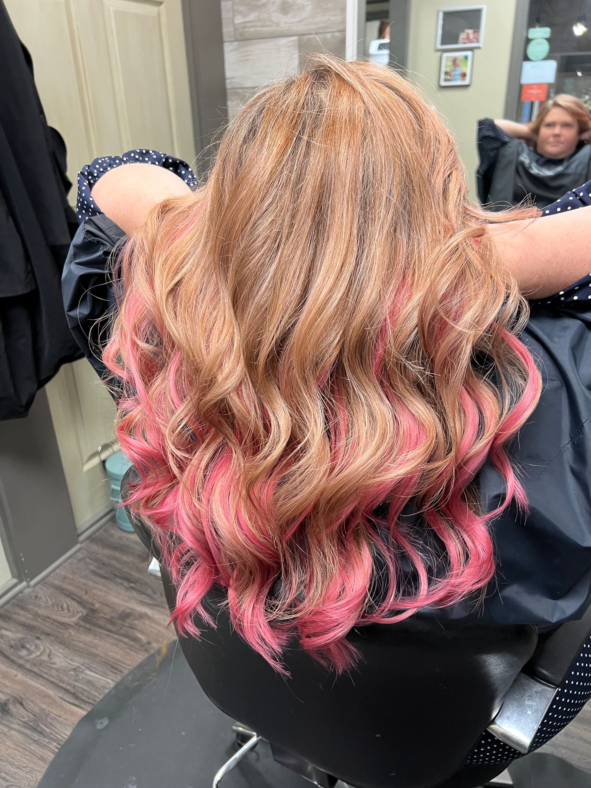 A woman with pink hair is sitting in a chair at a hair salon.