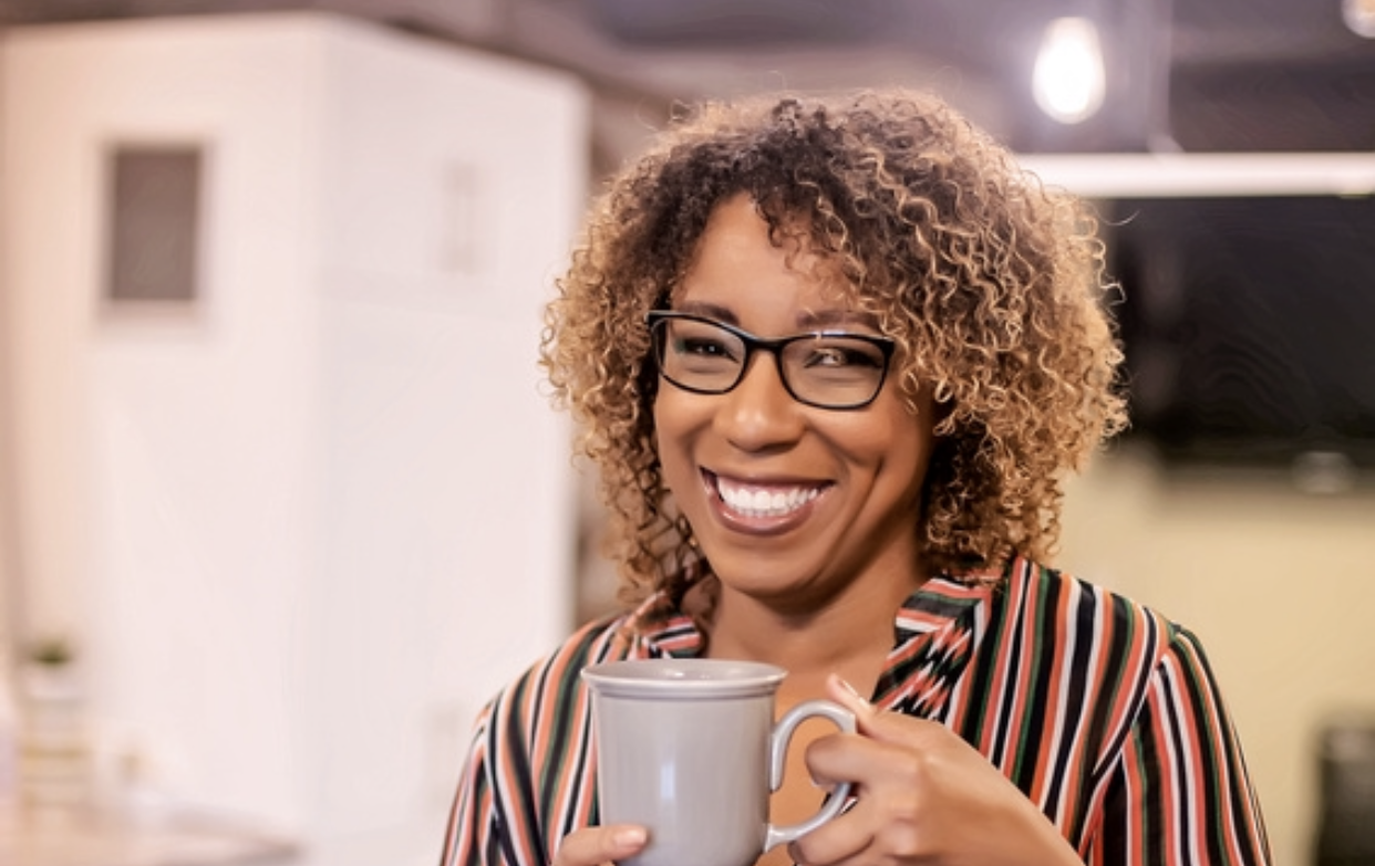 A woman wearing glasses is holding a cup of coffee and smiling.
