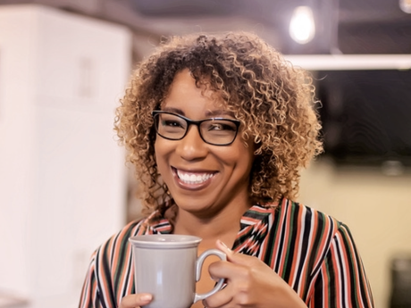 A woman wearing glasses is holding a cup of coffee and smiling.
