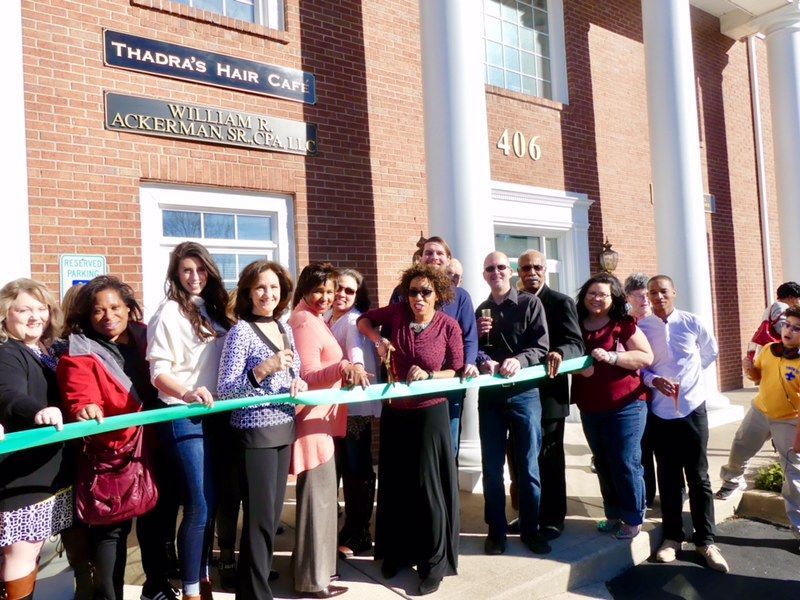 A group of people are cutting a green ribbon in front of a brick building