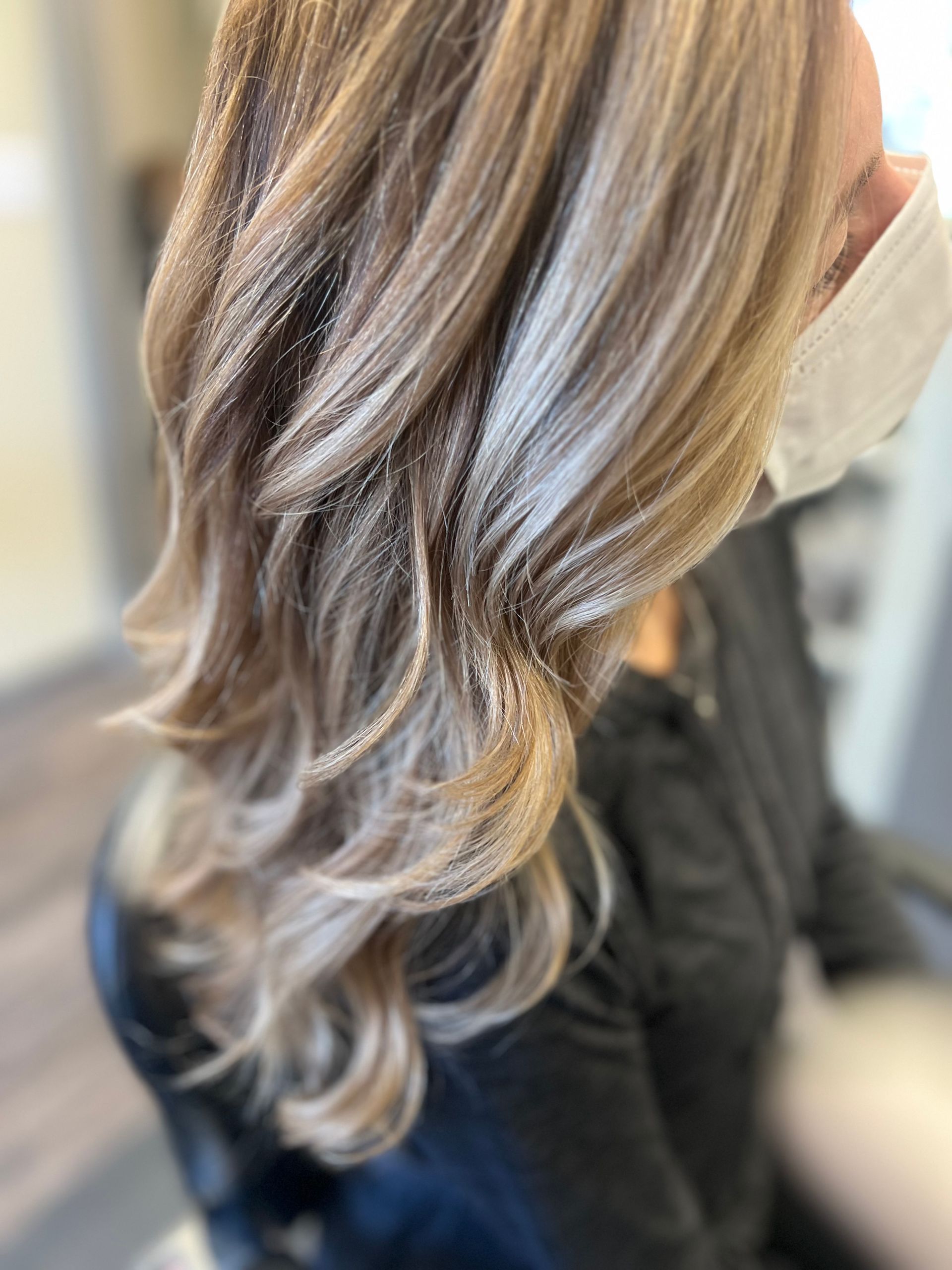 A woman with long blonde hair is wearing a black shirt and sitting in a chair.